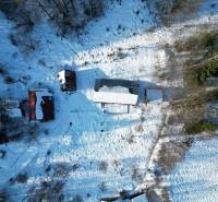 A snow-covered cottage in Veľké Rovné surrounded by trees and other buildings.