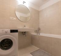 Bathroom in a 2-room apartment with a washing machine, bathtub, and beige tiles.