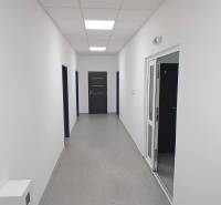 A narrow hallway in offices with white walls and a door at the end.