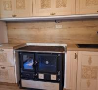 A kitchen unit with rustic cabinets, a black stove, and wooden paneling in a cabin.