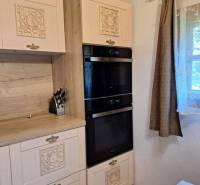 A kitchen in a cabin with carved cabinets, black appliances, and wooden decor.