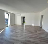 A spacious living room in a family house with wood-patterned flooring, large windows, and air conditioning.