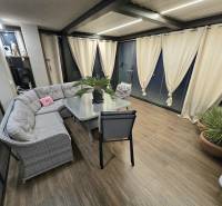 A covered terrace of a family house with a corner sofa and a floor with a wooden decor.