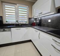 A kitchen in a family house with white cabinets, a dark countertop, and large windows.