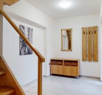 The hallway of a family house with wooden stairs, a chest of drawers, and a wall-mounted coat rack.