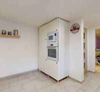 The kitchen part of a family house with a white cabinet, a shelf, and a clock on the wall.