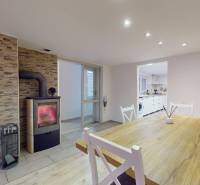 A dining room with a fireplace and wooden floor decor, connected to the kitchen in a family house.