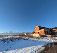 Family houses in Mlynica with snow-covered Tatras in the background under a clear blue sky.