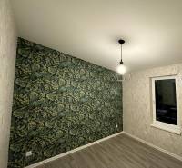 A room in a family house with a wooden decor floor and wallpaper with a tropical pattern.