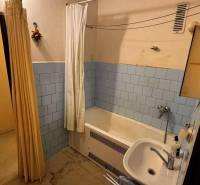 A bathroom with a bathtub and a sink in a 2-room apartment, tiled with light blue tiles.