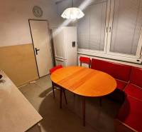 A kitchen in a 2-room apartment with a corner sofa, table, and white kitchen unit.