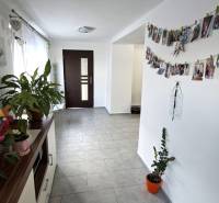 A hallway in a family house with flowers, photographs, and dark doors at the end.