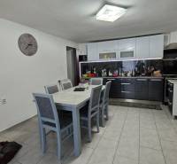 A kitchen in a family house with a dining table, chairs, white furniture, and a wall clock.