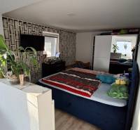 Bedroom with wood-patterned flooring, bed, flowers, and television in a family house.