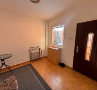 Interior of a family house with tiles, a table, a carpet, and a cabinet near the entrance.