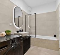 A bathroom in a 2-room apartment with a washing machine, a bathtub, and a mirror with LED lighting.