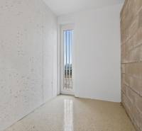 A hallway in a 2-room apartment with white walls and a brick wall.