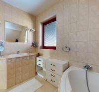 A bathroom in a family house with a corner bathtub, light tiles, and a sink.