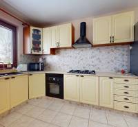 A kitchen in a family house with cream cabinets, a large window, and a stainless steel refrigerator.