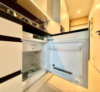 Kitchen area of a studio apartment with an open refrigerator and light-colored furniture.