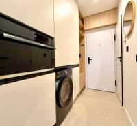 Entrance hallway with a washing machine, built-in oven, and white cabinets in a studio apartment.