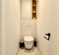 A toilet in a one-room apartment with white walls and built-in shelves.