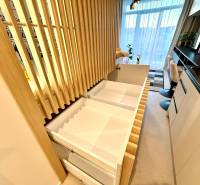 Interior of a 1-room apartment with wood decor, drawers, and a large window with white curtains.
