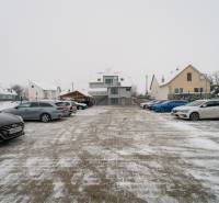 Snow-covered parking lot near offices on Bratislavská Road in Trenčín, with a row of cars.