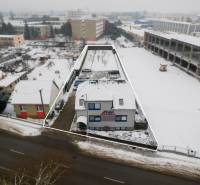 Snow-covered office buildings on Bratislavská Road in Trenčín with an adjacent parking lot.
