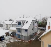 A snow-covered office building on Bratislavská Street in Trenčín with parked cars.