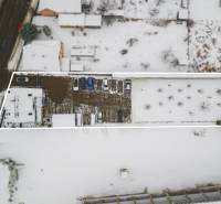 A snowy plot of land near Bratislavská Road in Trenčín, surrounded by offices and a parking lot.