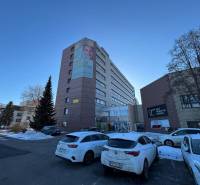 Office building in Poprad, snow-covered cars and road with blue sky.