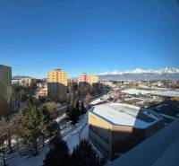 Poprad: apartment buildings, supermarkets, and snow-covered mountains behind offices under a clear sky.
