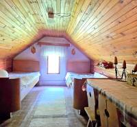 Attic room with wooden paneling, two beds, and a table in a family house.