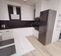 A kitchen in a 2-room apartment with white cabinets and a wooden decor floor.
