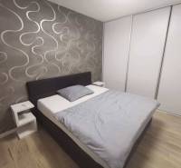 A bedroom in a two-room apartment with a wooden decor floor and wallpaper on the wall.