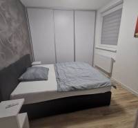 A bedroom in a two-room apartment with a wood-patterned floor and a built-in wardrobe.