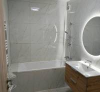 A bathroom with a bathtub, sink, and illuminated mirror in a 3-room apartment.