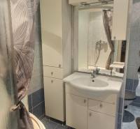 A bathroom in a studio apartment with blue tiles, a shower, and a white sink.