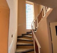 A staircase with a railing in a family house, illuminated by a large window with glass blocks.