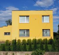 A yellow family house in Stretavka with a garden, surrounded by green bushes and a fence.