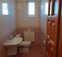 A bathroom with a sink and toilet, tiled with light tiles, in a family house.