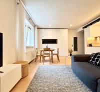 Living room with wood-patterned flooring and a kitchenette in a three-room apartment.