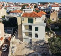 The exterior of a new building in the city of Trogir, surrounded by other houses and gardens.