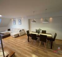 Living room in a three-room apartment with a wooden decor floor, dining table, and sofa.
