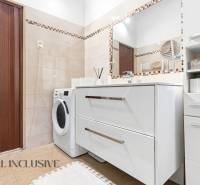 Bathroom in a family house with light tiles, a washing machine, and a mirror.