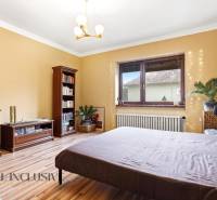 Bright bedroom with a bed, bookshelf, dresser, and wooden decor flooring in a family house.