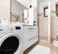 A bathroom in a family house with a washing machine, sink, mirror, and toilet, beige tiles.