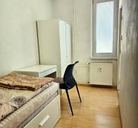 A simple room with a bed, a table, and a floor with a wooden decor in a two-room apartment.