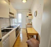 A kitchen in a 2-room apartment with appliances, a table, and a wooden decor floor.